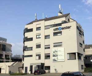 Het crèmekleurige gebouw van Officenter telt vijf verdiepingen. De naam 'Officenter' staat hoog op de gevel in zwarte letters. Allen de 'c' is lichtblauw.