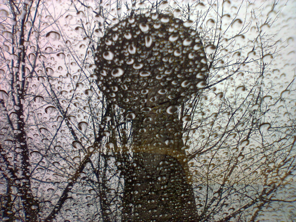De iconische VRT-toren van onderaf gefotografeerd door het glazen dak van m'n auto, dat vol druppels zit van de regen