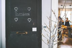 Het woord 'bonjour' in wit schoolkrijt op een grijze deur met daaromheen vier hartjes getekend